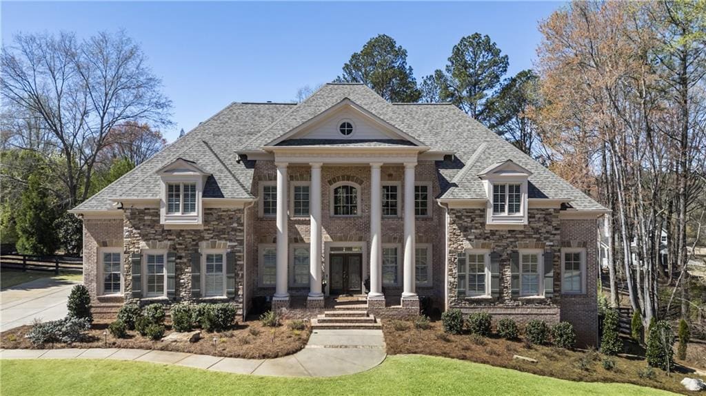 greek revival inspired property featuring brick siding, fence, french doors, and roof with shingles
