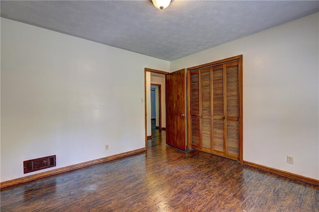 unfurnished bedroom featuring baseboards, wood finished floors, visible vents, and a textured ceiling