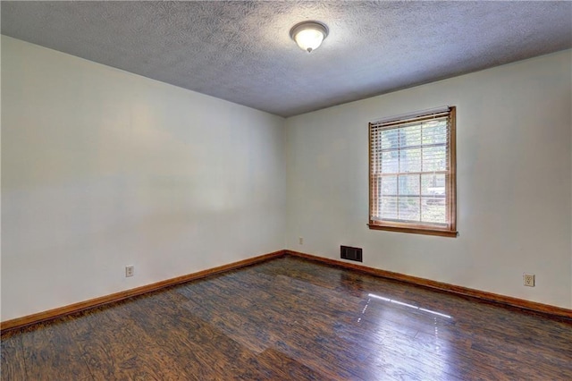 spare room with a textured ceiling, wood finished floors, visible vents, and baseboards