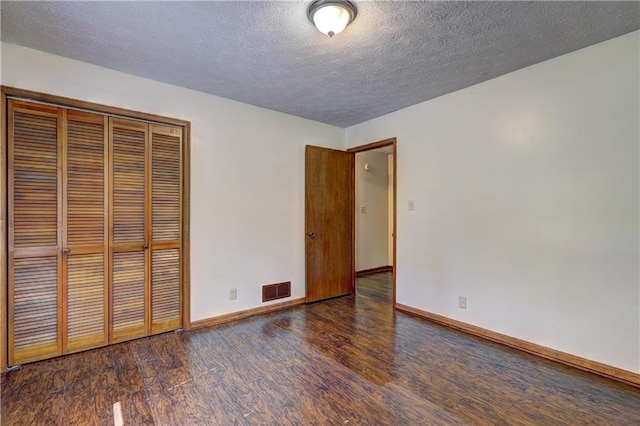 unfurnished bedroom with a textured ceiling, visible vents, baseboards, wood finished floors, and a closet