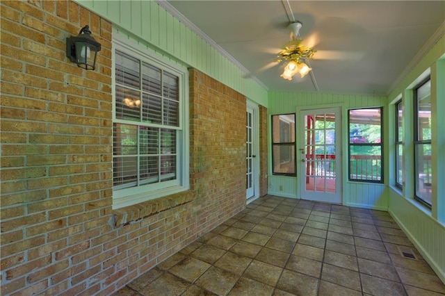 unfurnished sunroom featuring ornamental molding, visible vents, a ceiling fan, and brick wall