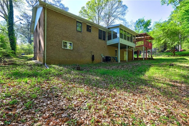 rear view of property featuring central AC unit, brick siding, a lawn, a deck, and a sunroom