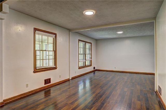 unfurnished room featuring visible vents, baseboards, a textured ceiling, and dark wood finished floors