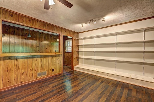 empty room with a textured ceiling, visible vents, wood walls, and a ceiling fan