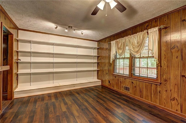 empty room with wooden walls, wood finished floors, visible vents, crown molding, and a textured ceiling