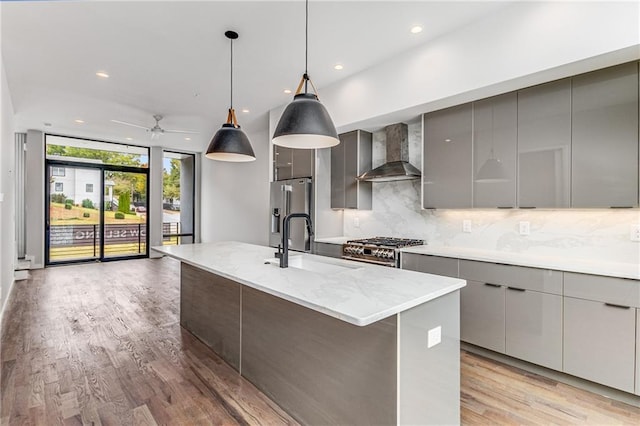 kitchen with an island with sink, decorative backsplash, wall chimney range hood, high quality appliances, and pendant lighting