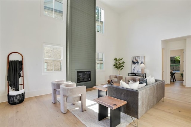 living room featuring a fireplace, a towering ceiling, light hardwood / wood-style flooring, and a healthy amount of sunlight