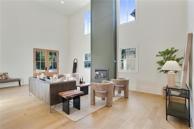 living room with a large fireplace, french doors, a wealth of natural light, and light hardwood / wood-style flooring