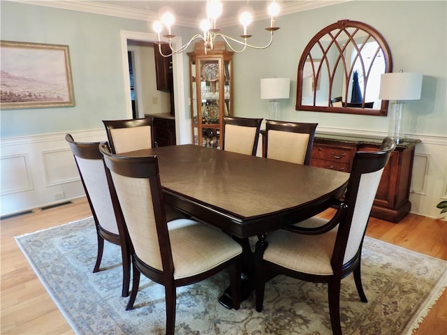 dining room with light wood-style flooring, a notable chandelier, a decorative wall, wainscoting, and ornamental molding