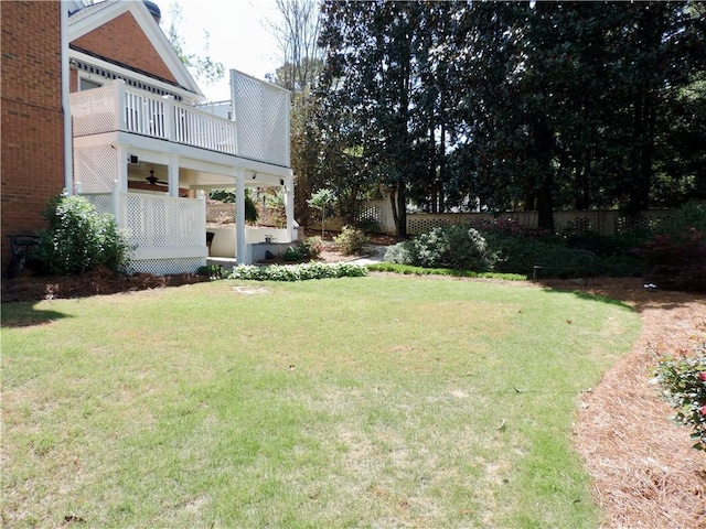view of yard featuring fence, a ceiling fan, and a balcony