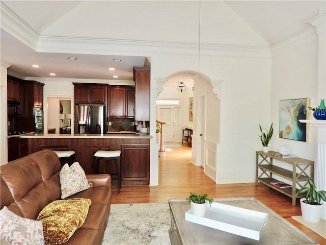 living area featuring ornamental molding, light wood-style flooring, lofted ceiling, and arched walkways