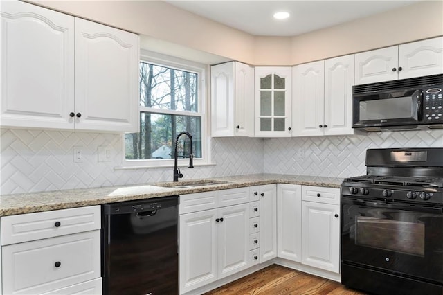 kitchen with white cabinetry, sink, light stone counters, black appliances, and light hardwood / wood-style flooring