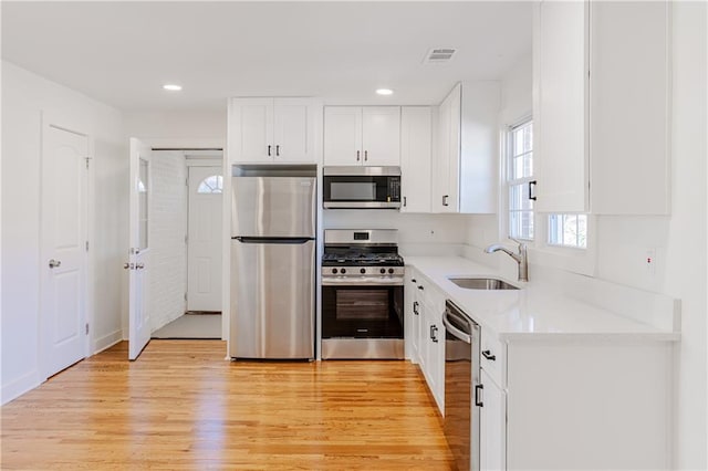 kitchen with stainless steel appliances, white cabinetry, sink, and light wood-type flooring