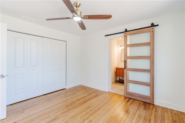 unfurnished bedroom featuring a closet, a barn door, ceiling fan, and light wood-type flooring