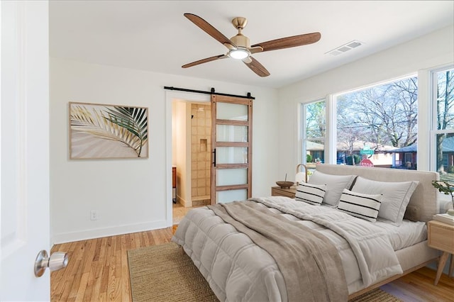 bedroom with ceiling fan, a barn door, and light hardwood / wood-style floors