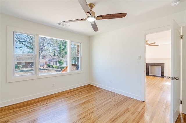 unfurnished room with a fireplace, ceiling fan, and light wood-type flooring