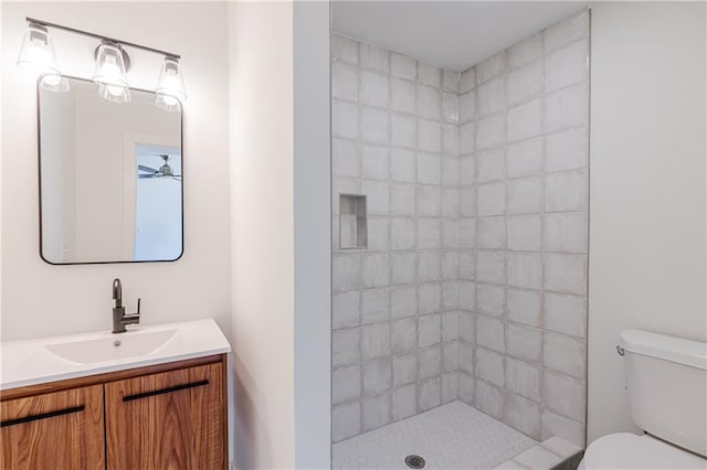 bathroom featuring vanity, tiled shower, ceiling fan, and toilet