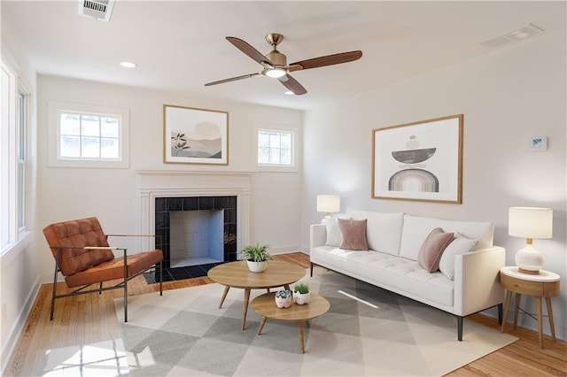 living room with a tiled fireplace, light hardwood / wood-style floors, and ceiling fan