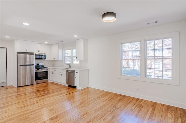 kitchen with stainless steel appliances, white cabinetry, sink, and light wood-type flooring