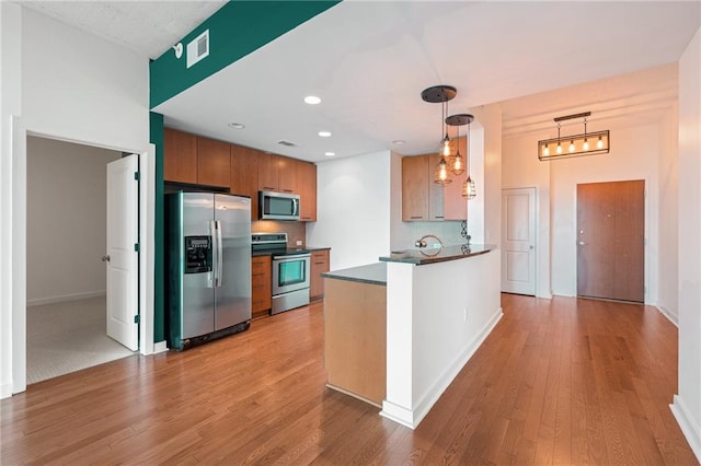 kitchen featuring pendant lighting, light wood-type flooring, tasteful backsplash, kitchen peninsula, and stainless steel appliances