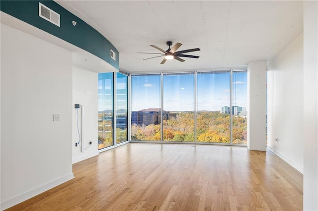 empty room with ceiling fan, expansive windows, and light hardwood / wood-style floors