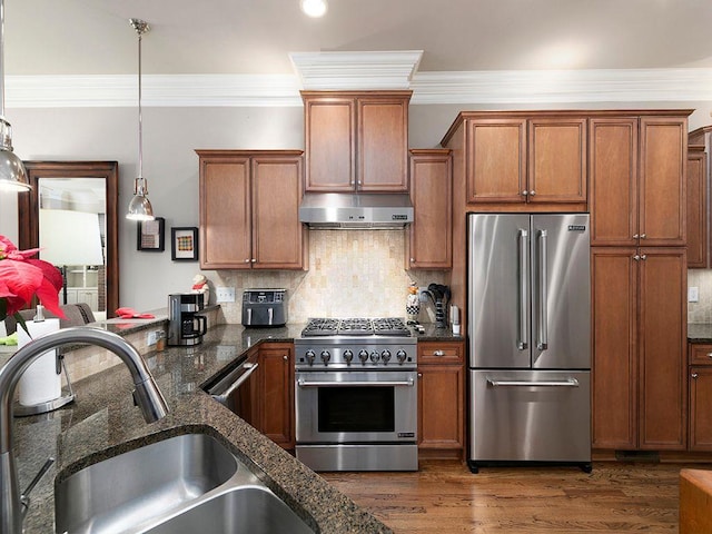 kitchen featuring under cabinet range hood, dark wood-type flooring, a sink, high quality appliances, and brown cabinets