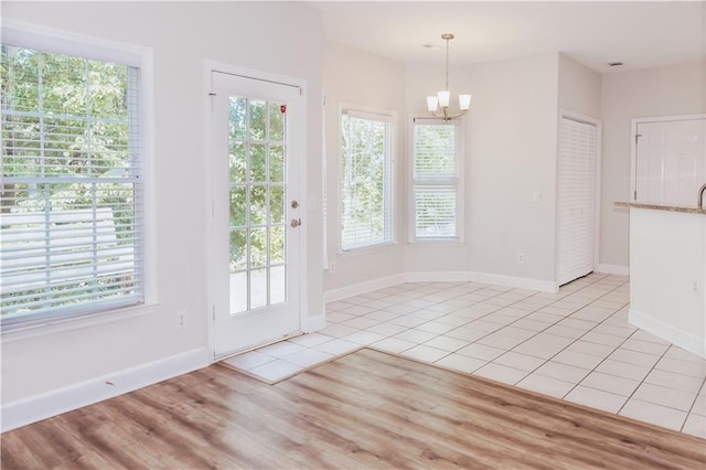 unfurnished dining area with a chandelier, plenty of natural light, and baseboards
