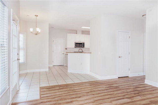kitchen featuring stainless steel microwave, a chandelier, white cabinets, decorative light fixtures, and light wood finished floors