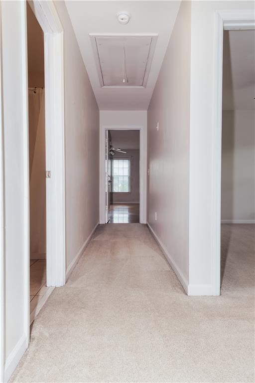 corridor featuring attic access, light colored carpet, and baseboards