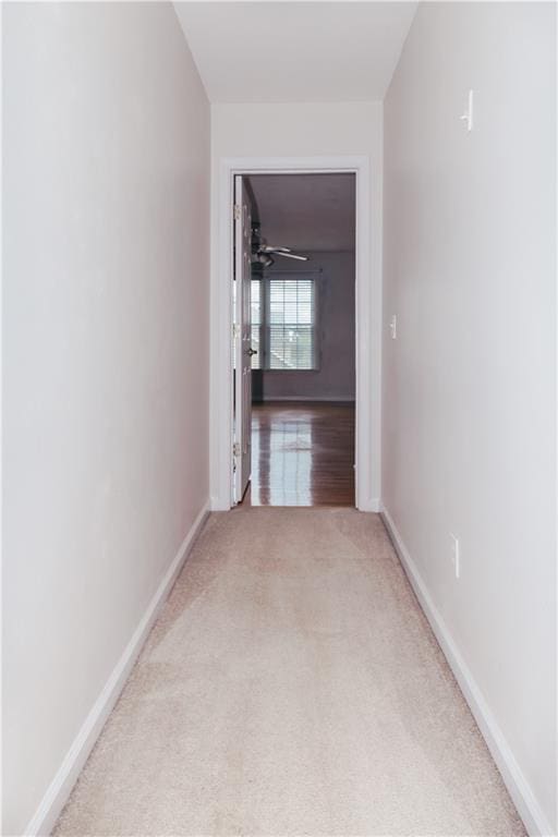 hallway featuring light carpet and baseboards