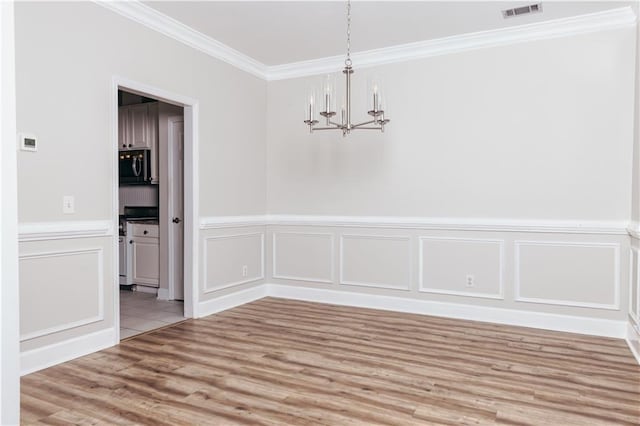 unfurnished dining area featuring a chandelier, ornamental molding, light wood finished floors, a decorative wall, and wainscoting