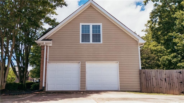 garage with concrete driveway and fence