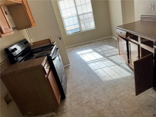 kitchen with brown cabinetry, range with electric cooktop, dark countertops, and baseboards