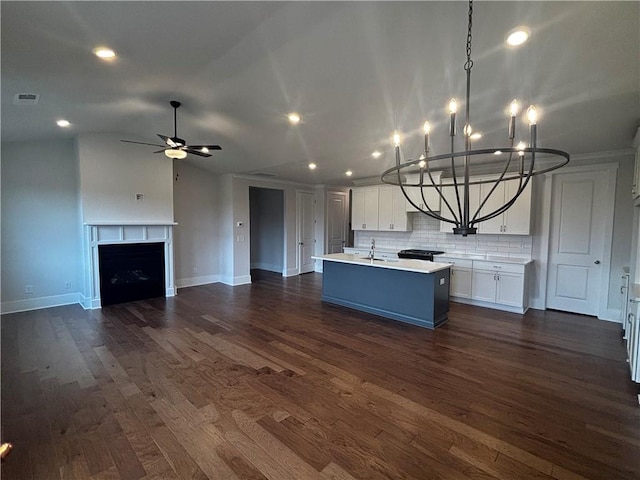 kitchen with backsplash, sink, an island with sink, white cabinets, and dark wood-type flooring