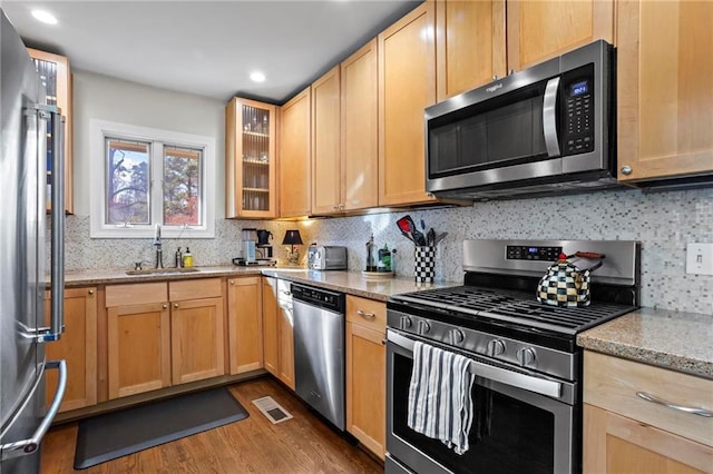 kitchen with light stone counters, a sink, visible vents, appliances with stainless steel finishes, and glass insert cabinets