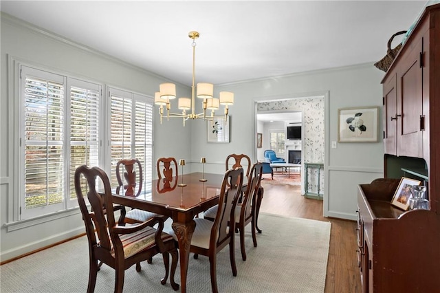 dining space with baseboards, wood finished floors, an inviting chandelier, crown molding, and a fireplace