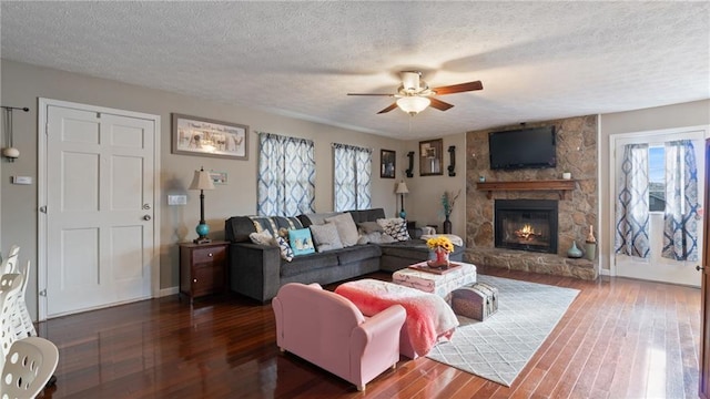 living area featuring a wealth of natural light, a stone fireplace, and dark wood-type flooring