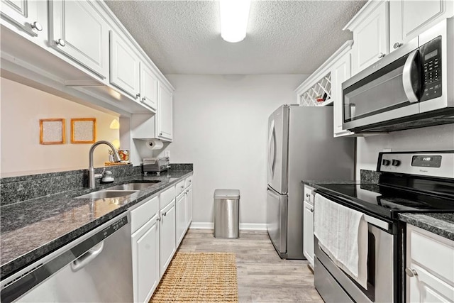 kitchen featuring dark stone countertops, stainless steel appliances, sink, and white cabinets