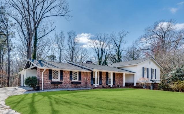 split level home featuring a front yard, brick siding, driveway, and a chimney