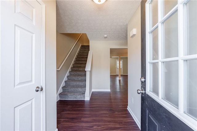 foyer entrance featuring a textured ceiling, stairs, baseboards, and wood finished floors