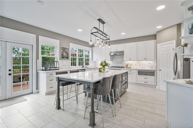 1775 Porterton Way, Cumming, GA 30041 - kitchen with a warming drawer, under cabinet range hood, a breakfast bar area, decorative backsplash, and light countertops