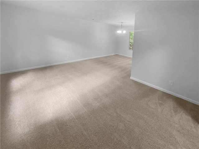 spare room featuring carpet floors, a chandelier, and baseboards