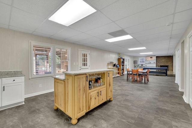 kitchen featuring a paneled ceiling, a center island, light brown cabinetry, and a brick fireplace