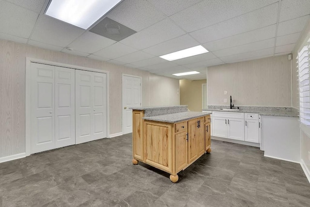 kitchen with a paneled ceiling, a center island, light stone countertops, and sink