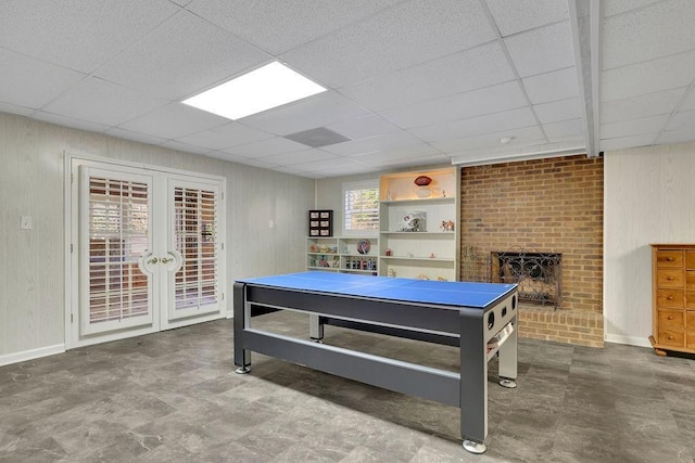 game room with a drop ceiling, french doors, and a brick fireplace