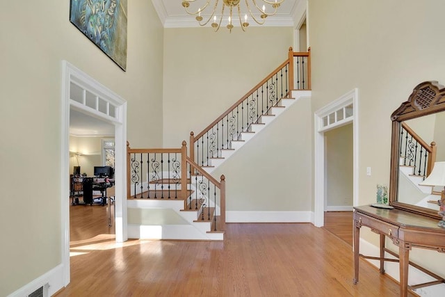 foyer with a high ceiling, wood-type flooring, a notable chandelier, and ornamental molding