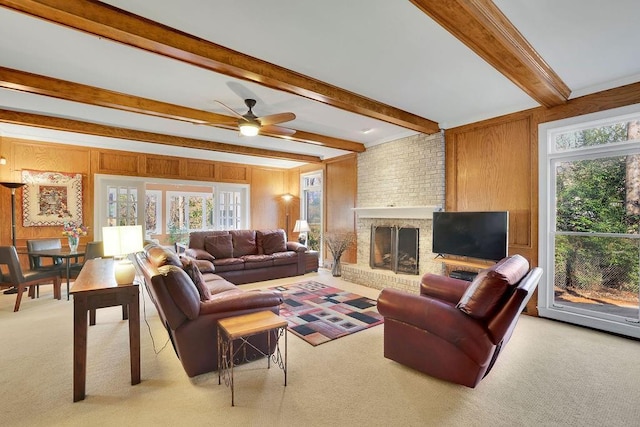 living room featuring wood walls, light carpet, a brick fireplace, ceiling fan, and beamed ceiling