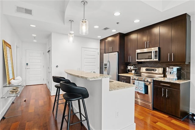 kitchen featuring a breakfast bar area, light wood-type flooring, appliances with stainless steel finishes, a kitchen island, and pendant lighting