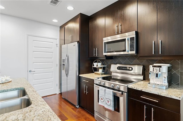 kitchen featuring dark brown cabinetry, appliances with stainless steel finishes, dark hardwood / wood-style flooring, light stone countertops, and decorative backsplash