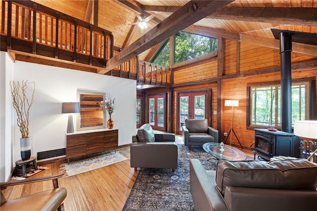 living room with ceiling fan, light wood-type flooring, wood ceiling, a wood stove, and wooden walls